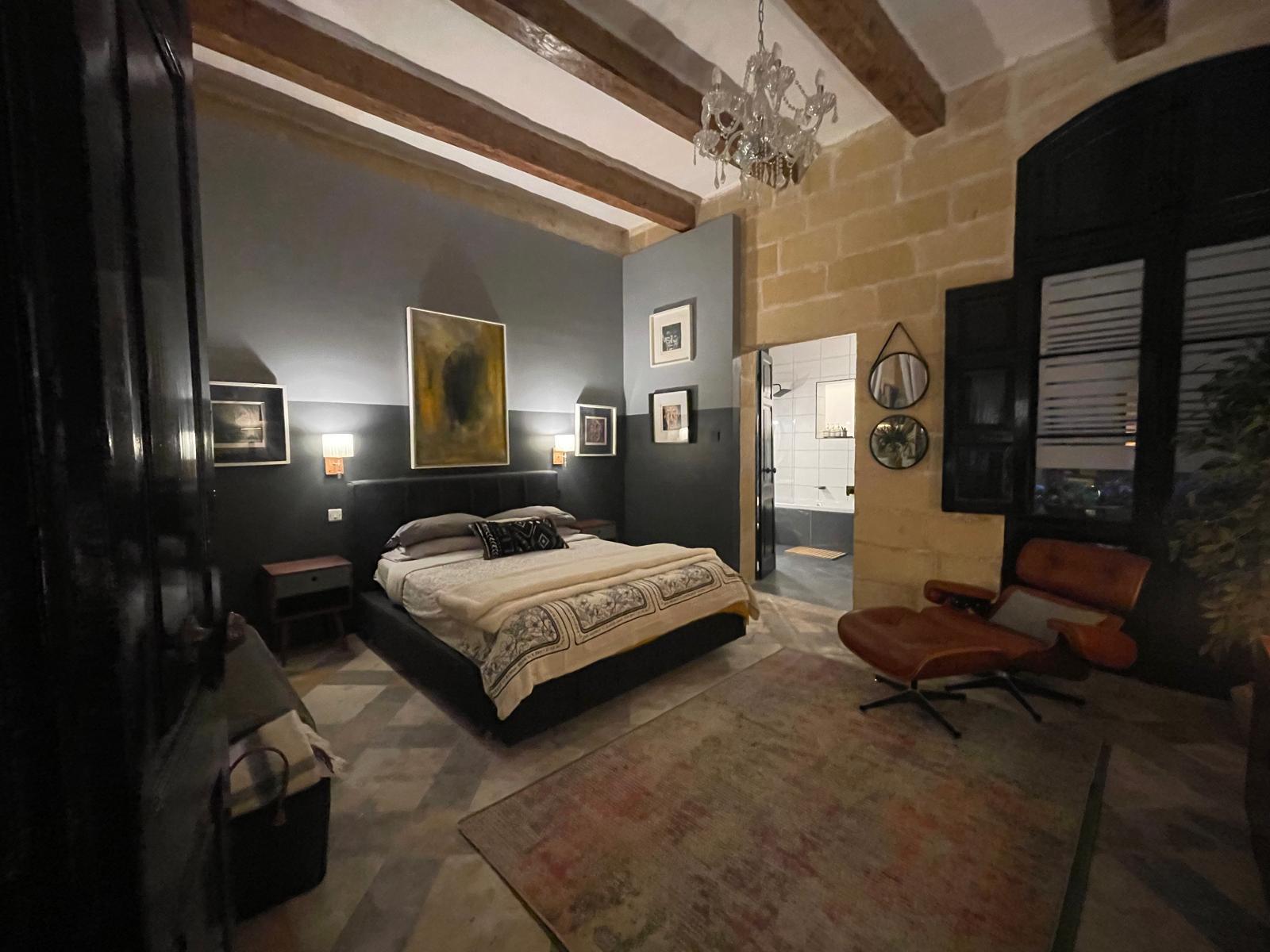 Bedroom with dark walls, a chandelier and a leather lounge chair