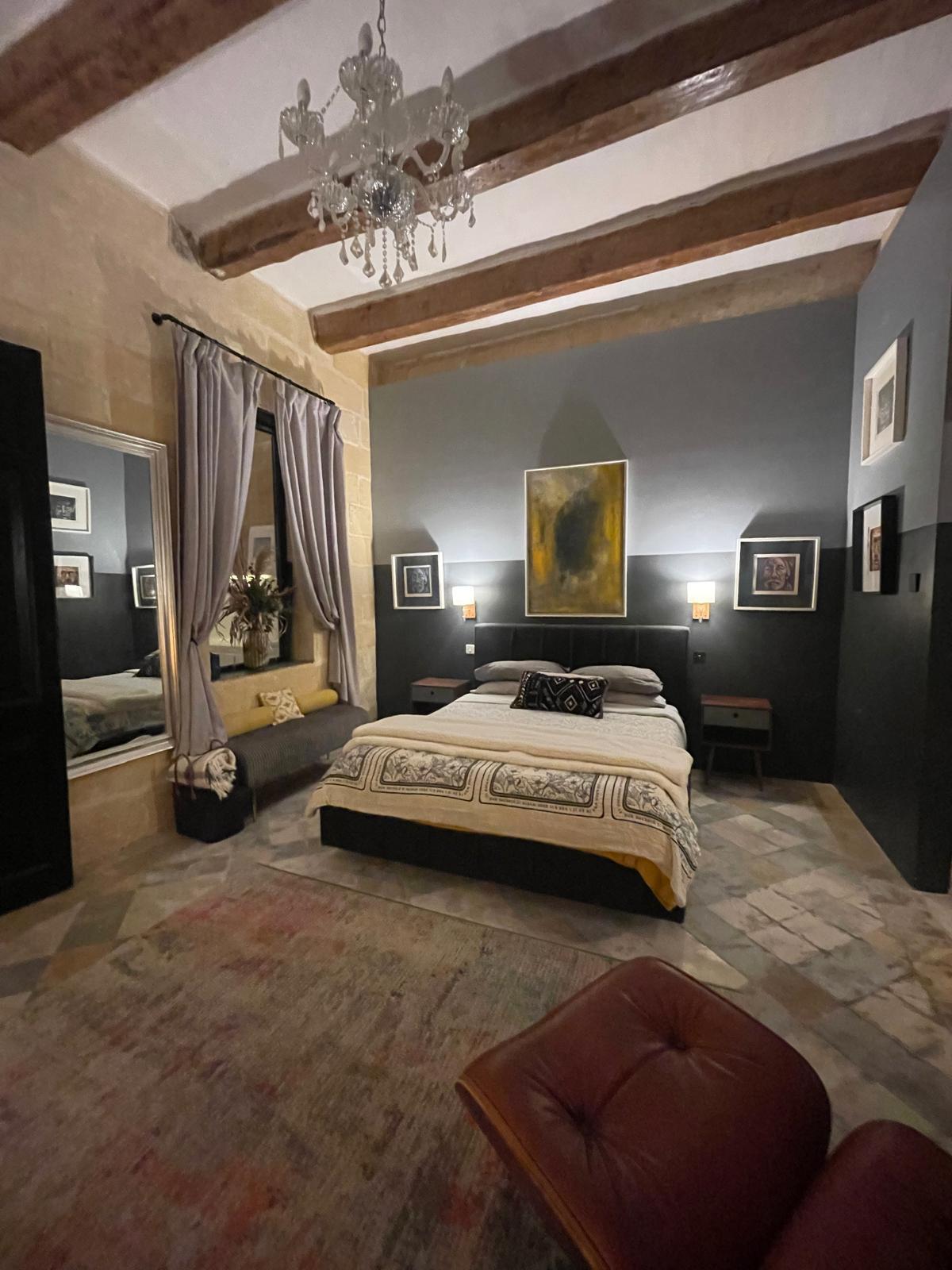 Bedroom seen from the doorway, under timber beams and a chandelier