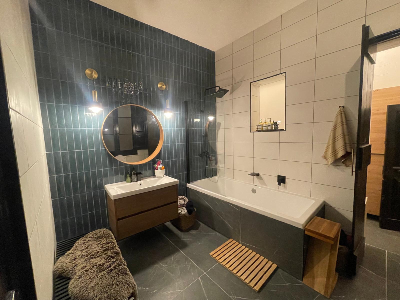 Bathroom with dark green tiles, a round mirror and a bath